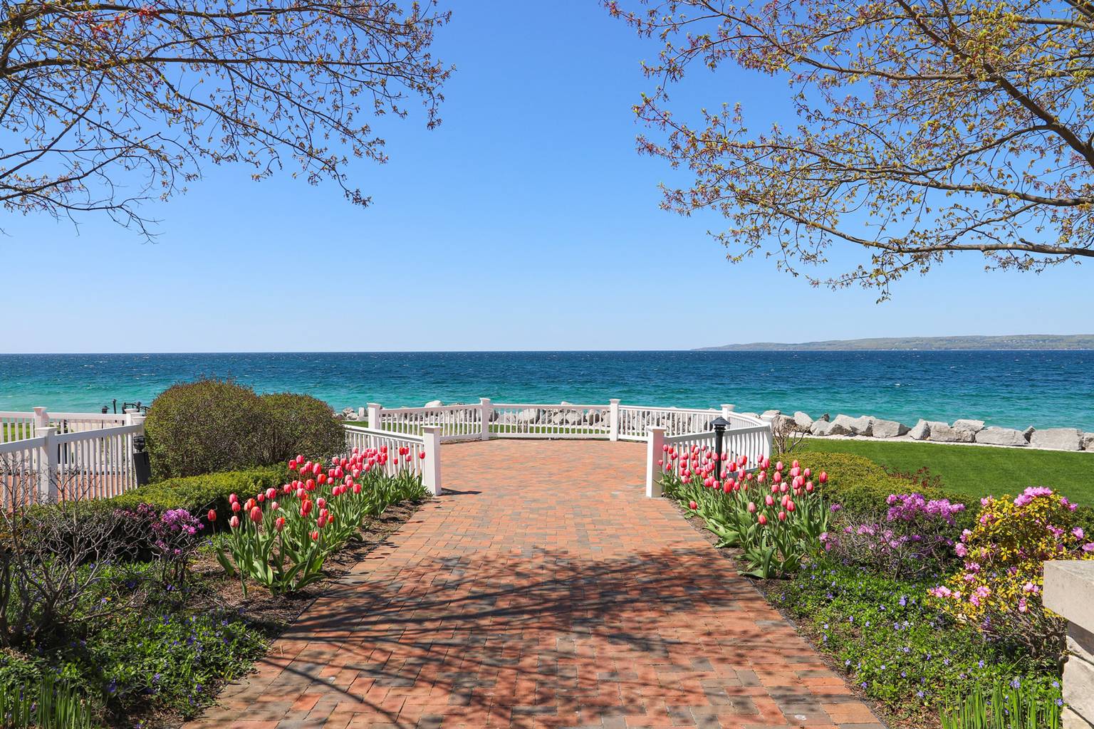 Tulips and budding trees surrounding Inn at Bay Harbor brick patio overlooking bright blue water of Lake Michigan