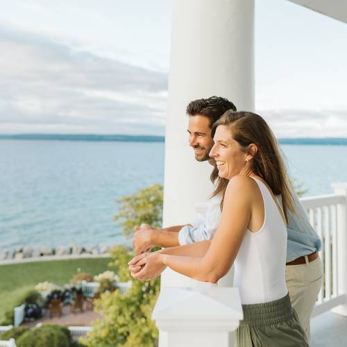 Smiling couple looks out over lakefront balcony on summer evening