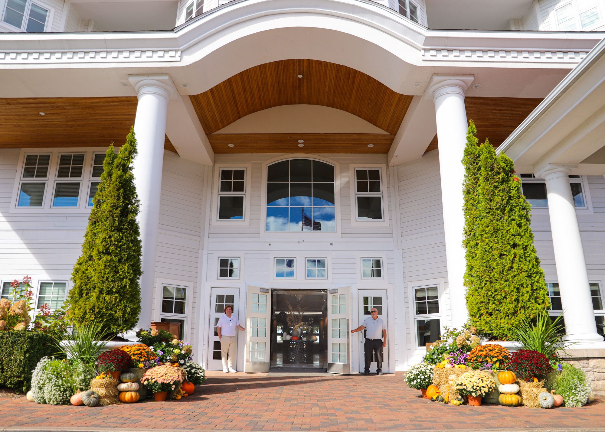 Valets hold doors open at front entrance of Inn at Bay Harbor, decorated for autumn with pumpkins, mums
