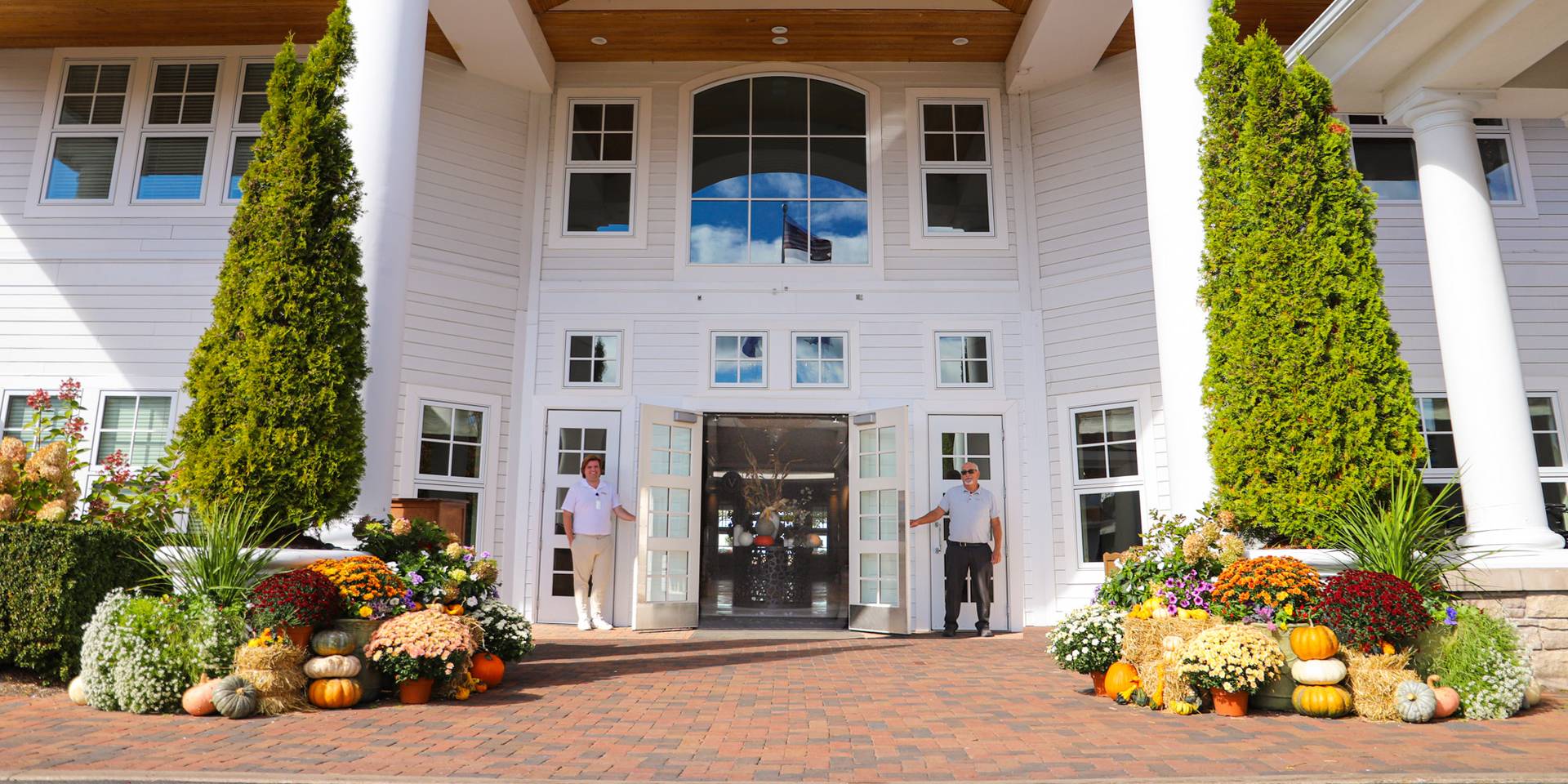 Valets hold doors open at front entrance of Inn at Bay Harbor, decorated for autumn with pumpkins, mums