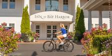 Blonde woman rides bicycle by colorful gardens at front entrance of Inn at Bay Harbor