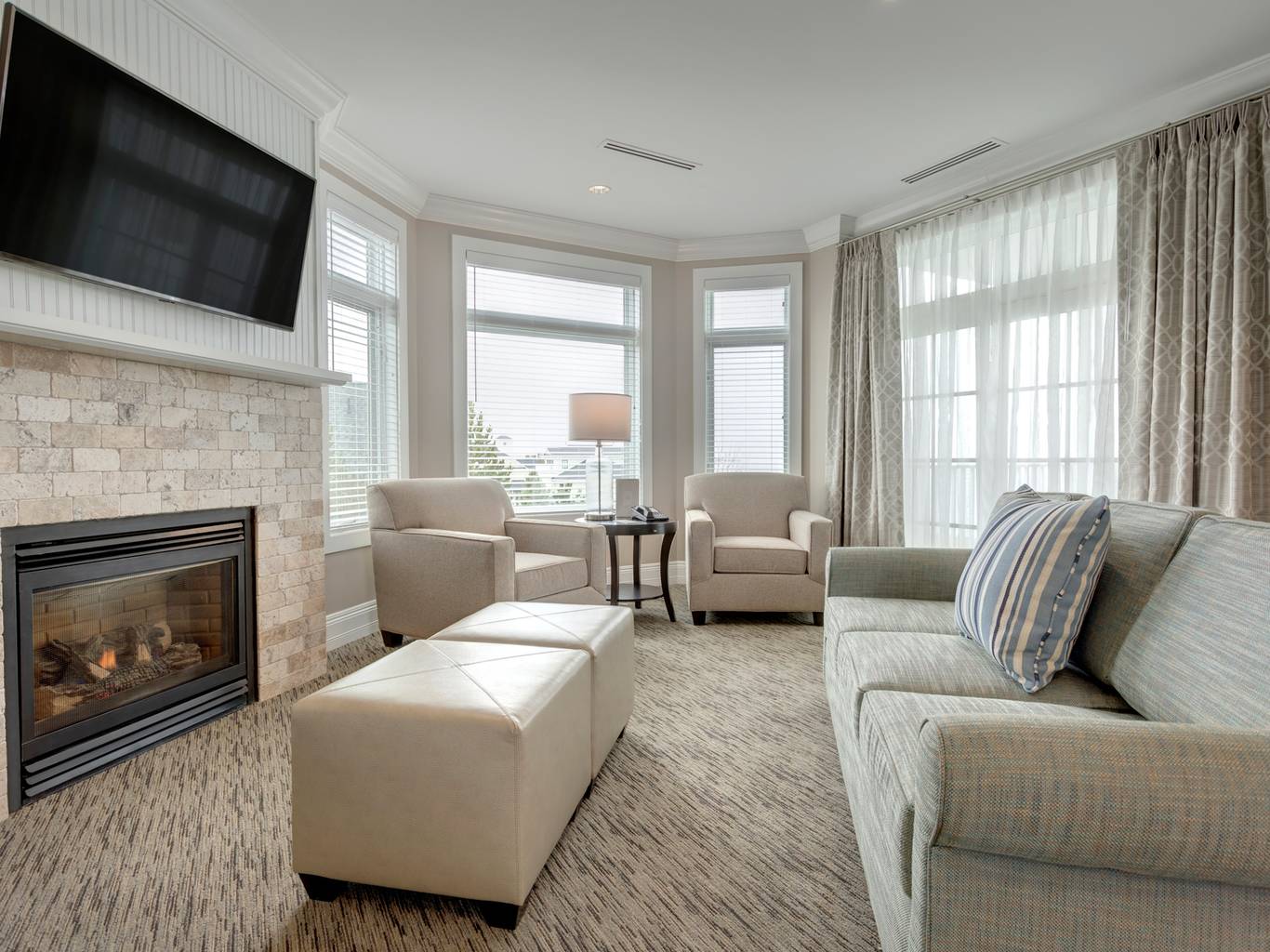 King Suite living area with neutral couch, ottomans, and fireplace near large windows, Inn at Bay Harbor