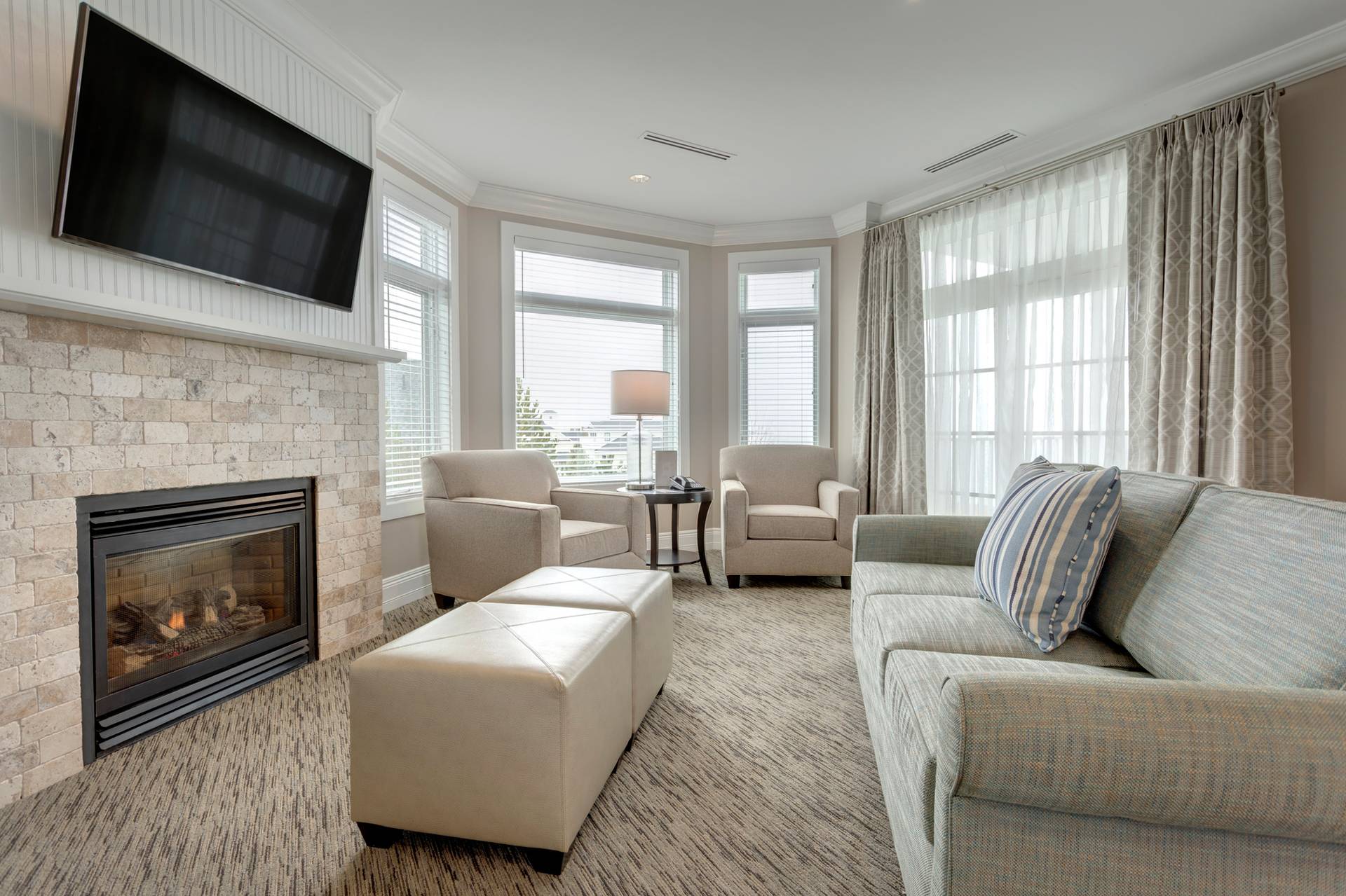 King Suite living area with neutral couch, ottomans, and fireplace near large windows, Inn at Bay Harbor