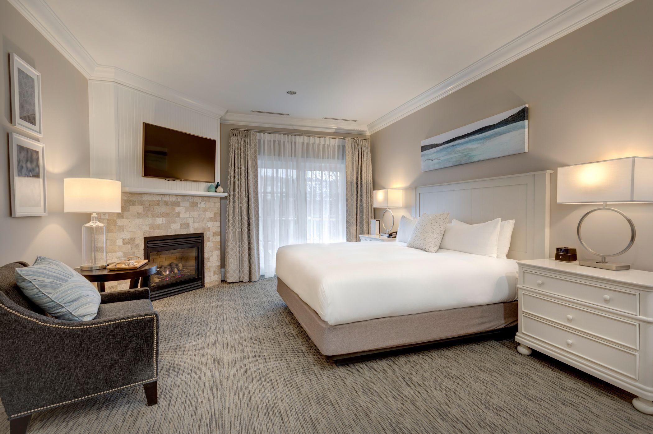 Grand King hotel room with white bed, neutral decor, dark chair near tile fireplace