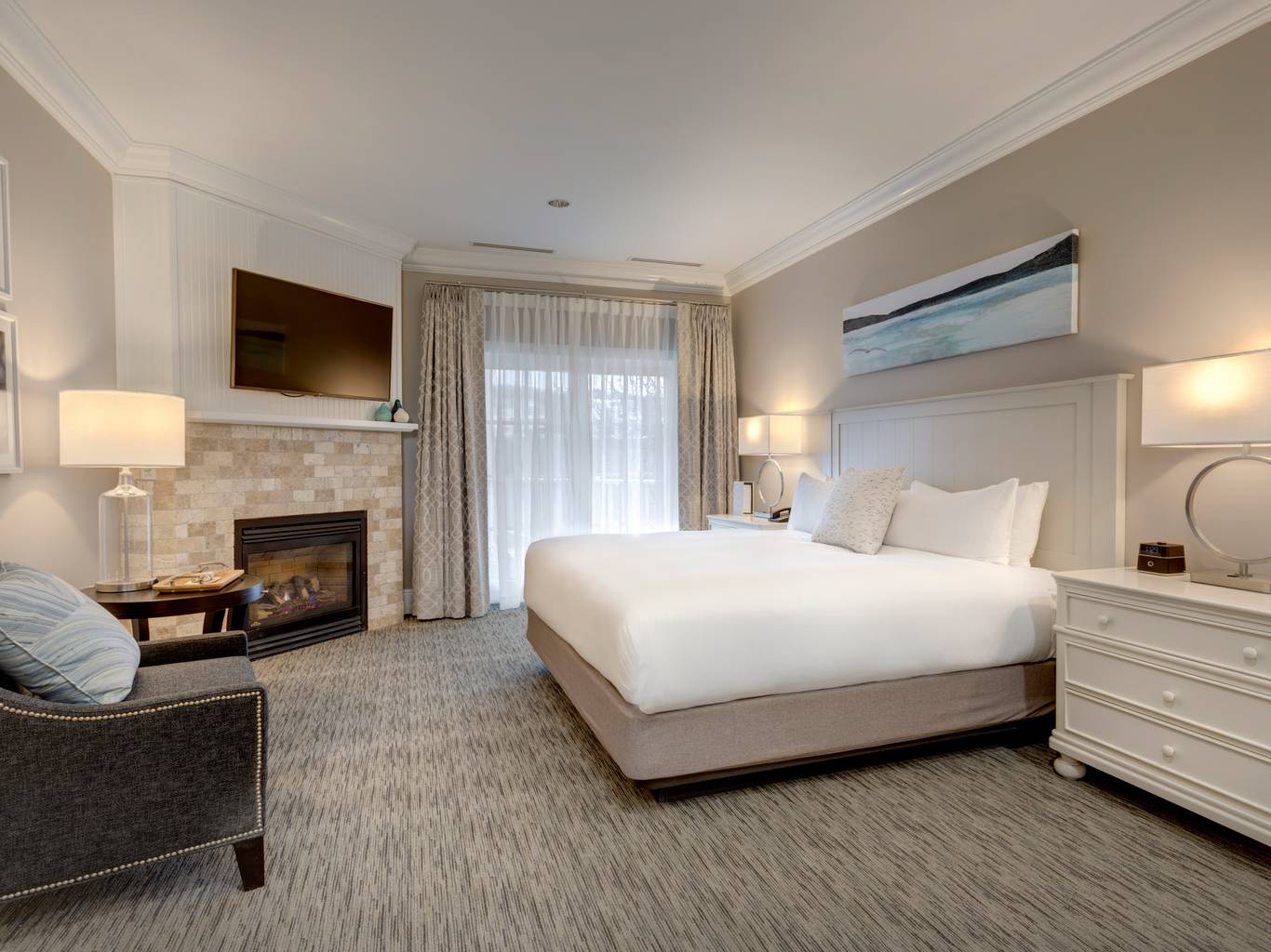 Grand King hotel room with white bed, neutral decor, dark chair near tile fireplace