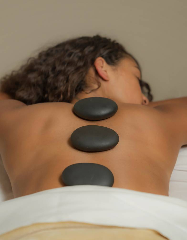 Hot black stones aligned on woman's bare back while she lays on hands at The Spa