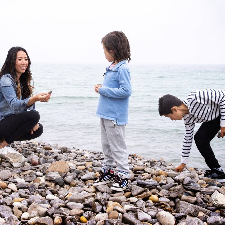 Young mother holds up rock to son as she and other son hunt for stones along rocky Lake Michigan shoreline