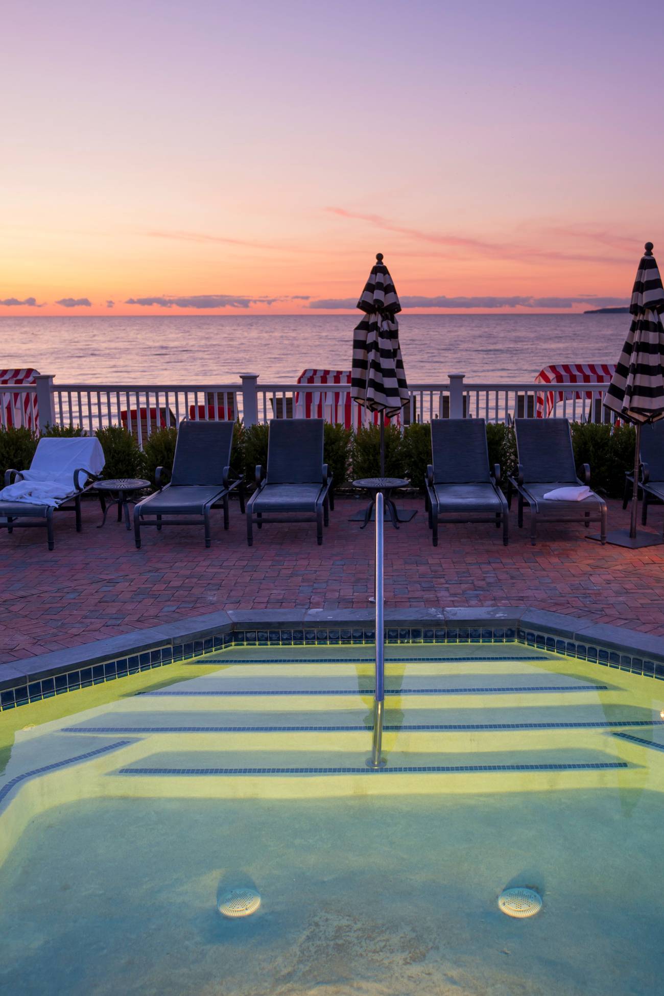 Evening lit hot tub surrounded by pool loungers in front sunset over Lake Michigan