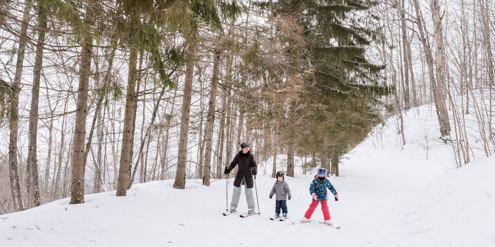 A mom and two kids ski down a trail at The Highlands ski area