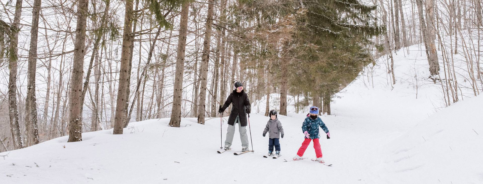 A mom and two kids ski down a trail at The Highlands ski area