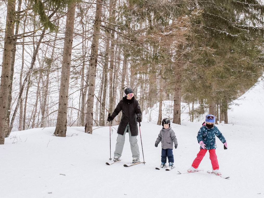 A mom and two kids ski down a trail at The Highlands ski area