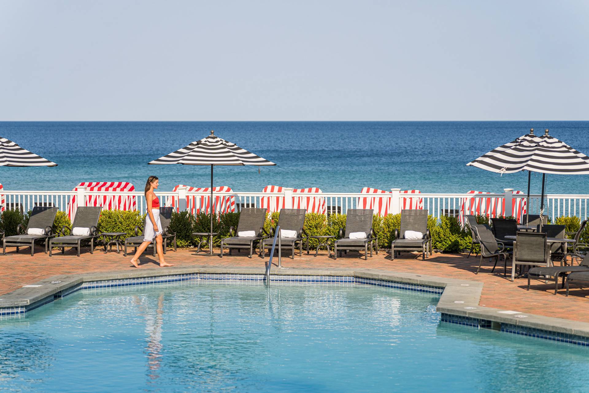 Blue waters of pool and Lake Michigan, with woman walking between on pool deck with striped umbrellas
