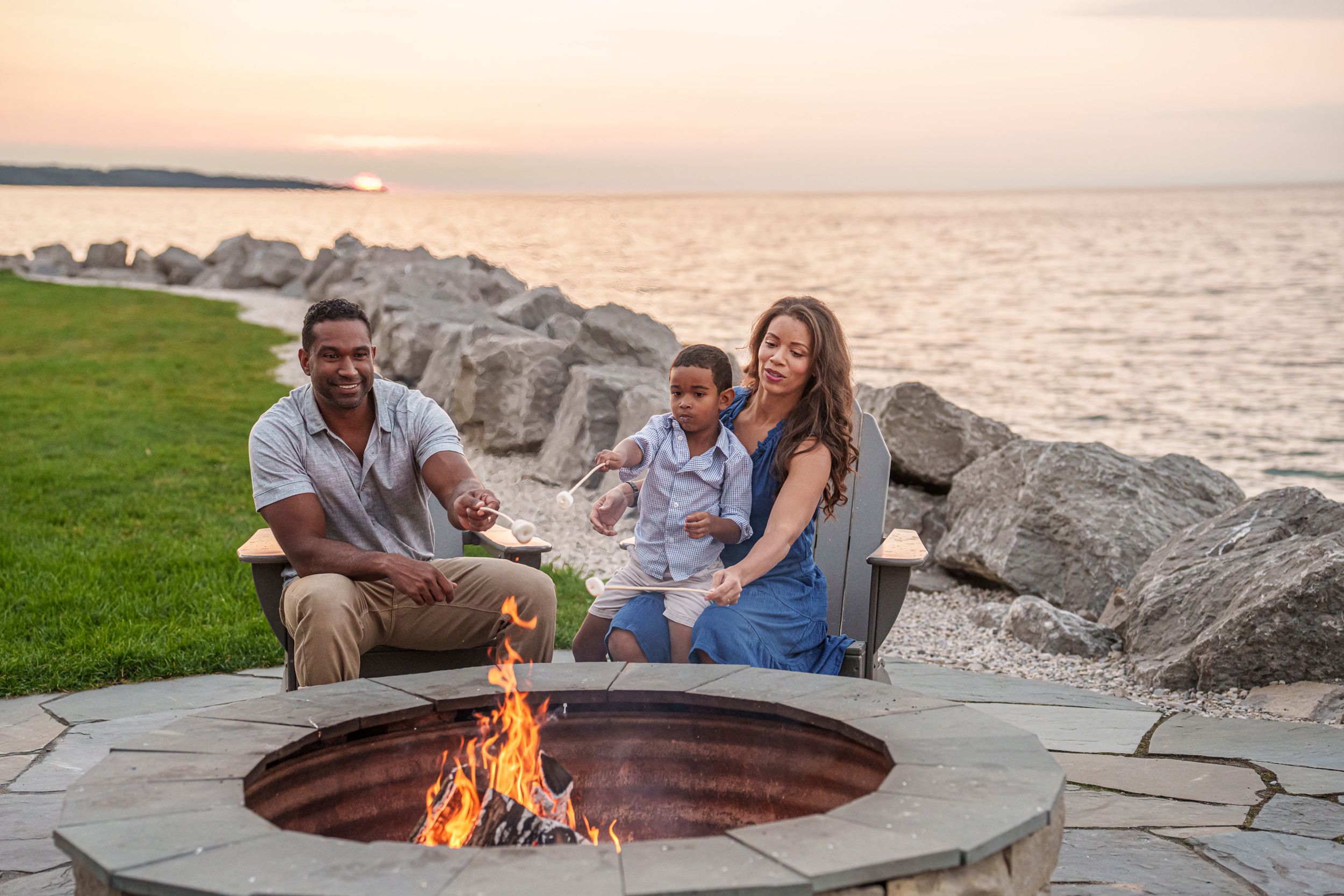Family makes s'mores at lakefront firepit under sunset sky