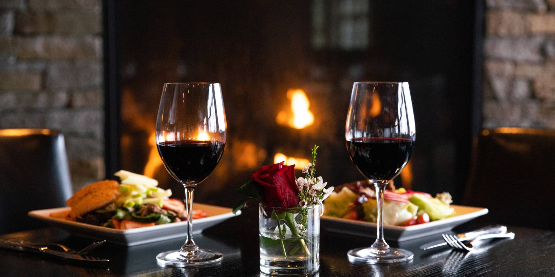 Detail of two red wine glasses with salads in front of stone fireplace, Vintage Chophouse | Wine Bar