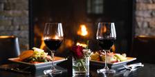 Detail of two red wine glasses with salads in front of stone fireplace, Vintage Chophouse | Wine Bar