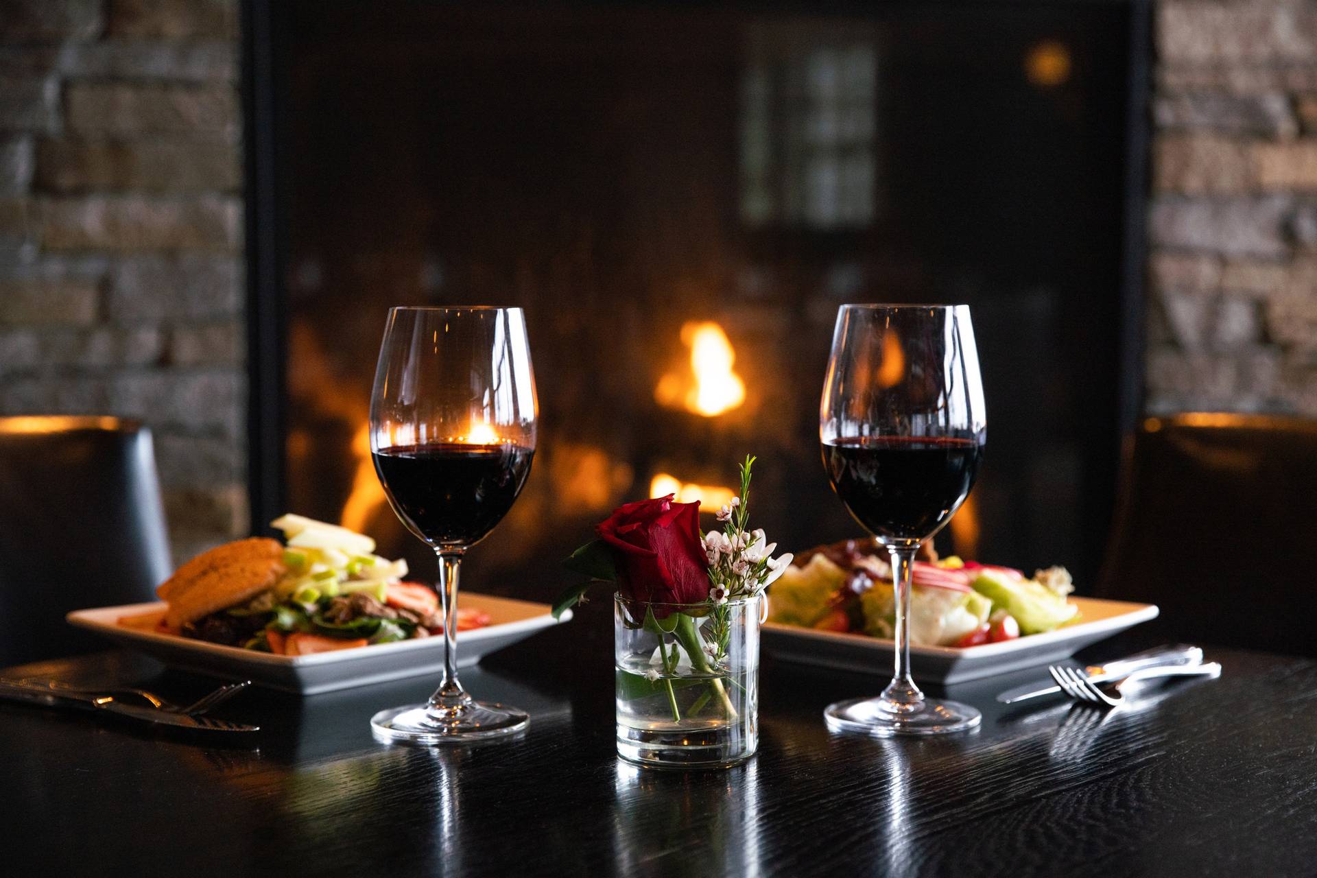 Detail of two red wine glasses with salads in front of stone fireplace, Vintage Chophouse | Wine Bar