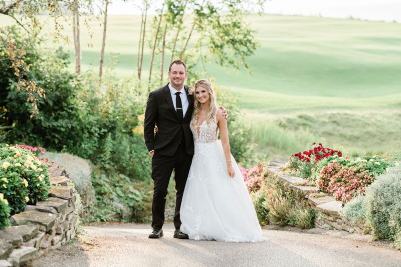 Bride and groom smile at camera while standing on garden path, Bay Harbor Golf Club