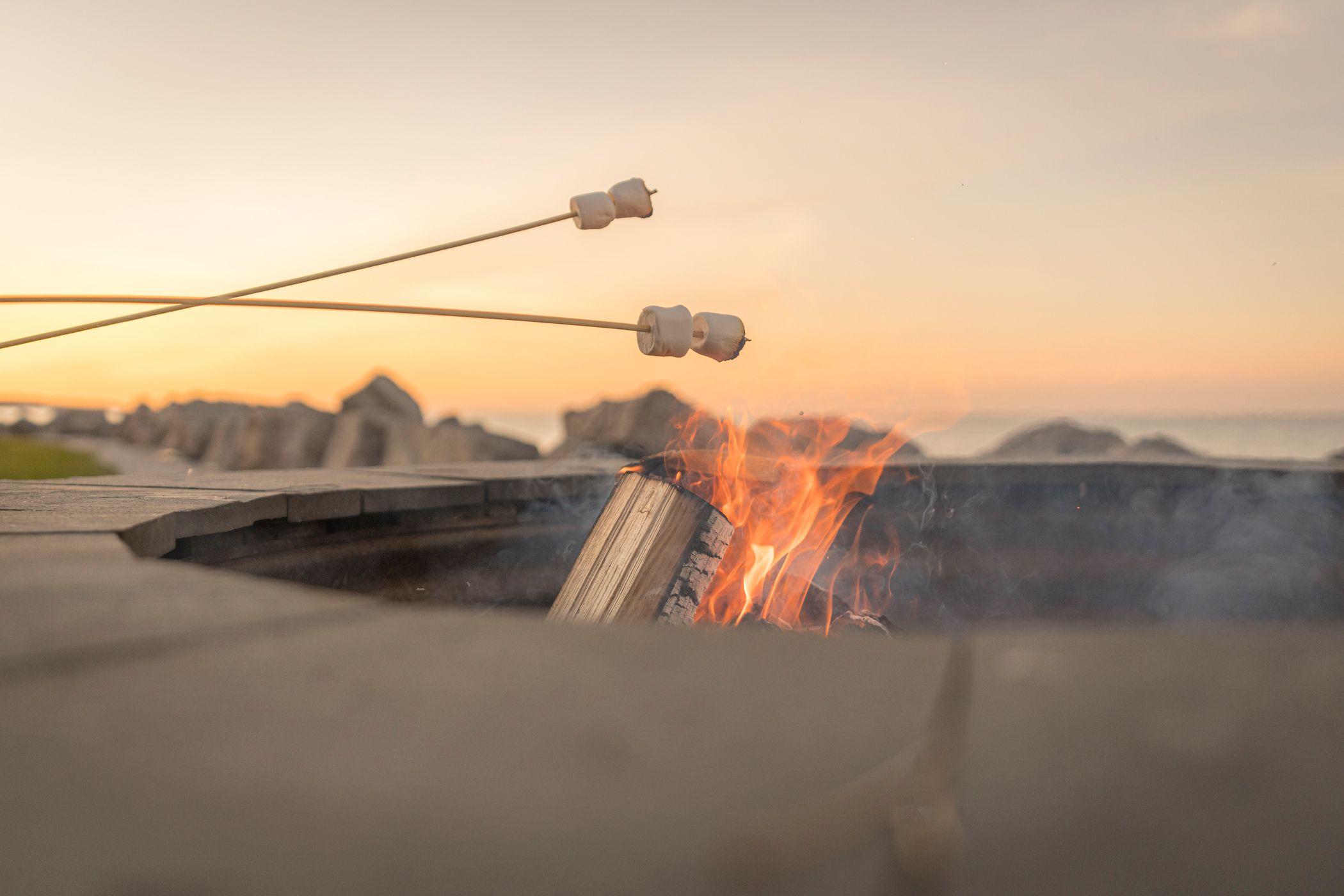 Detail of marshmallows roasting over lakefront bonfire under orange sunset sky