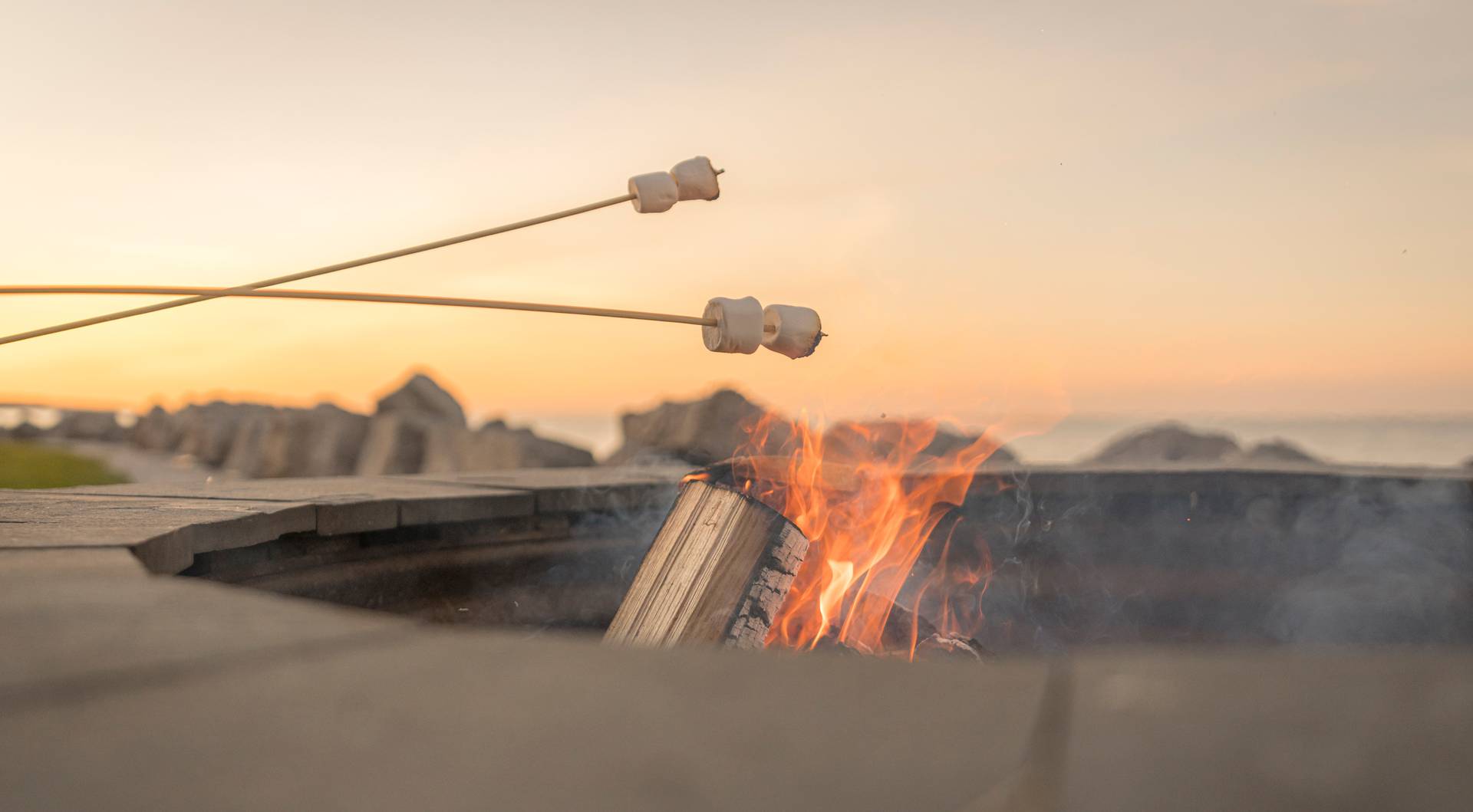 Detail of marshmallows roasting over lakefront bonfire under orange sunset sky