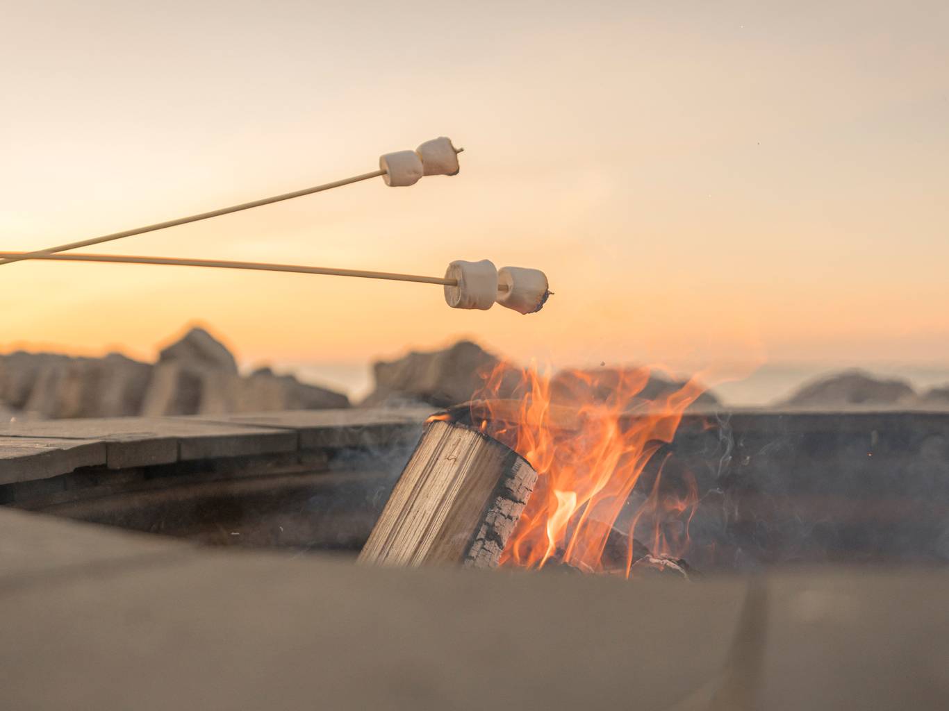 Detail of marshmallows roasting over lakefront bonfire under orange sunset sky