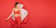 Smiling woman in red workout attire steps through red wrapping paper