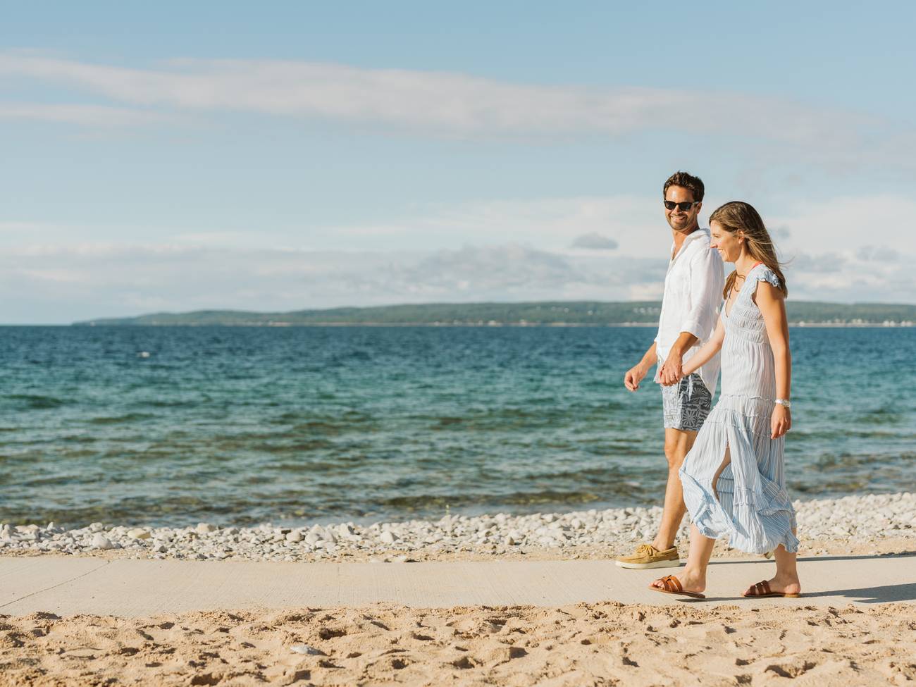 Smiling couple walks along summer beach sidewalk in front of Little Traverse Bay