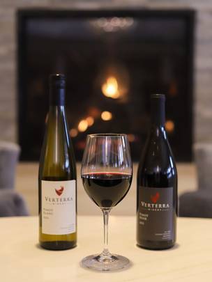 Glass of red wine, between Verterra red, white wine bottles near fireplace