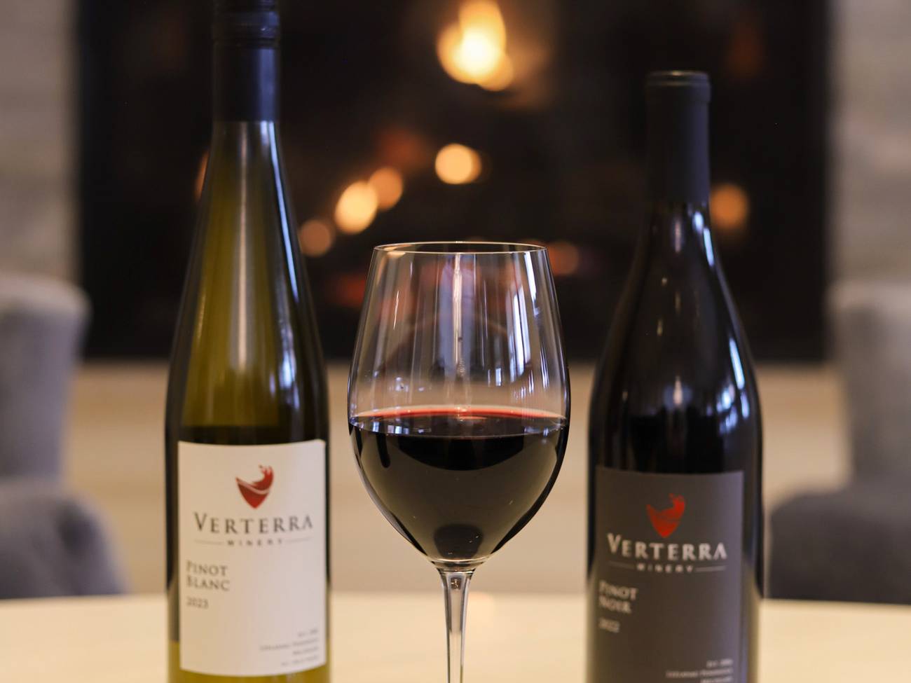 Glass of red wine, between Verterra red, white wine bottles near fireplace