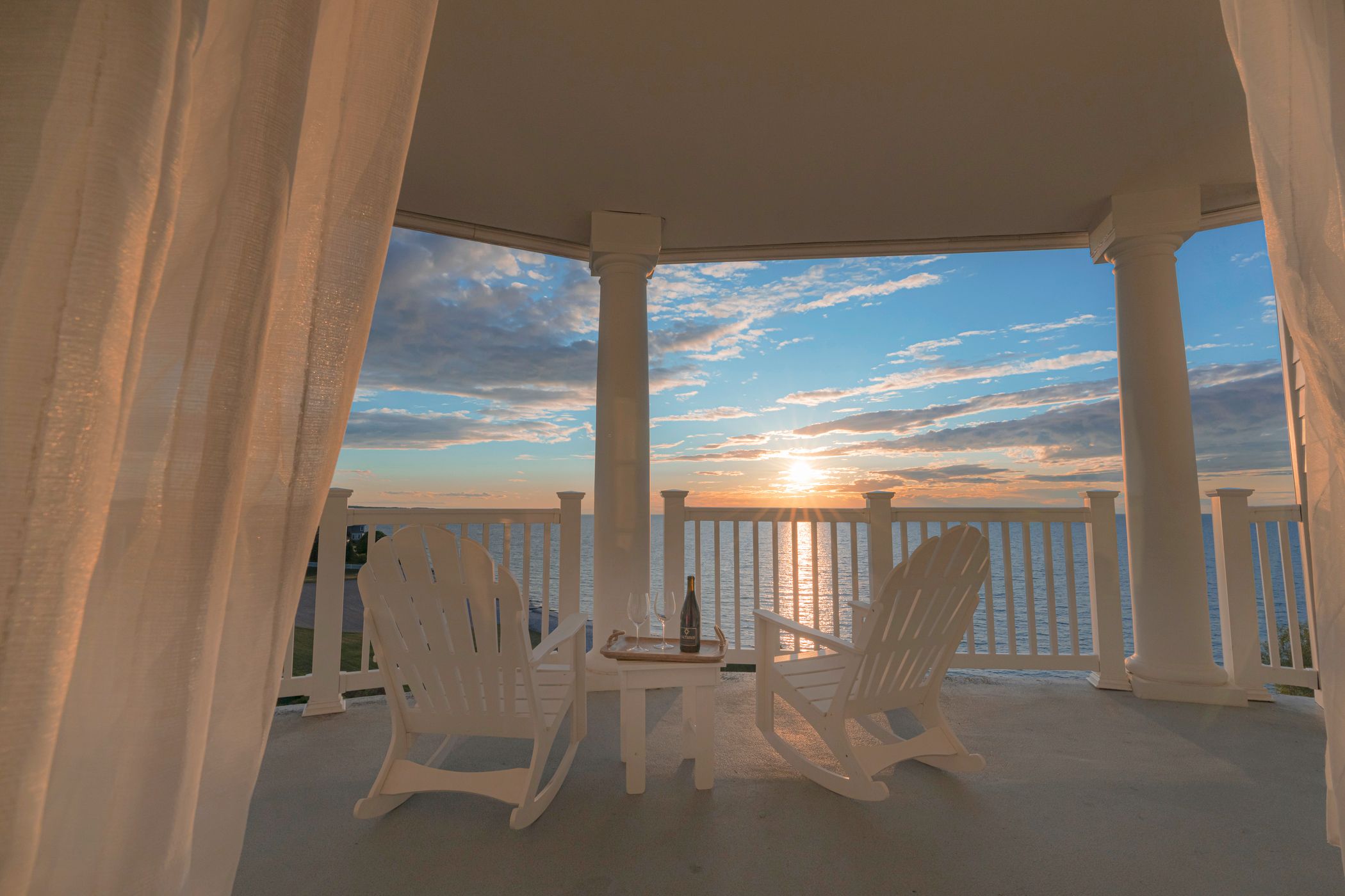 White Adirondack rocking chairs on balcony overlooking sunset on Lake Michigan
