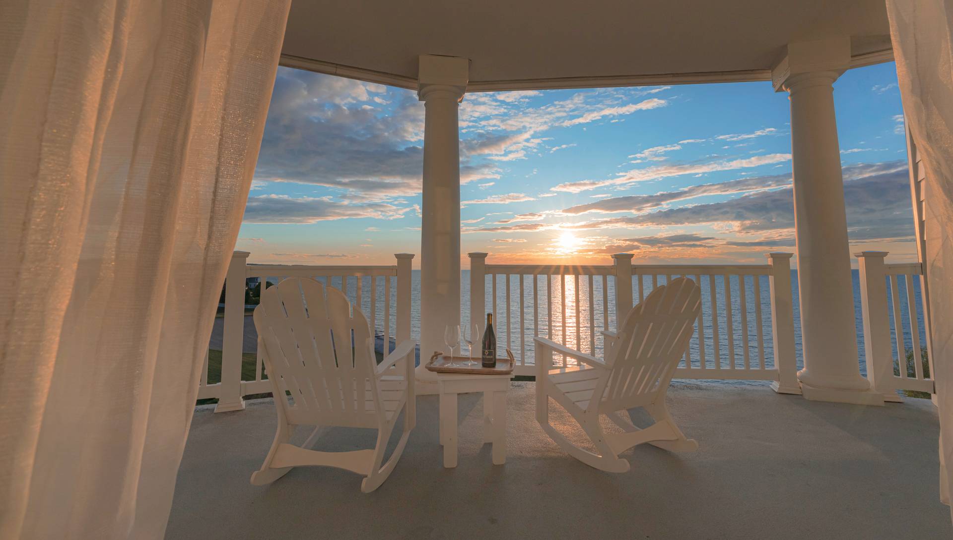 White Adirondack rocking chairs on balcony overlooking sunset on Lake Michigan
