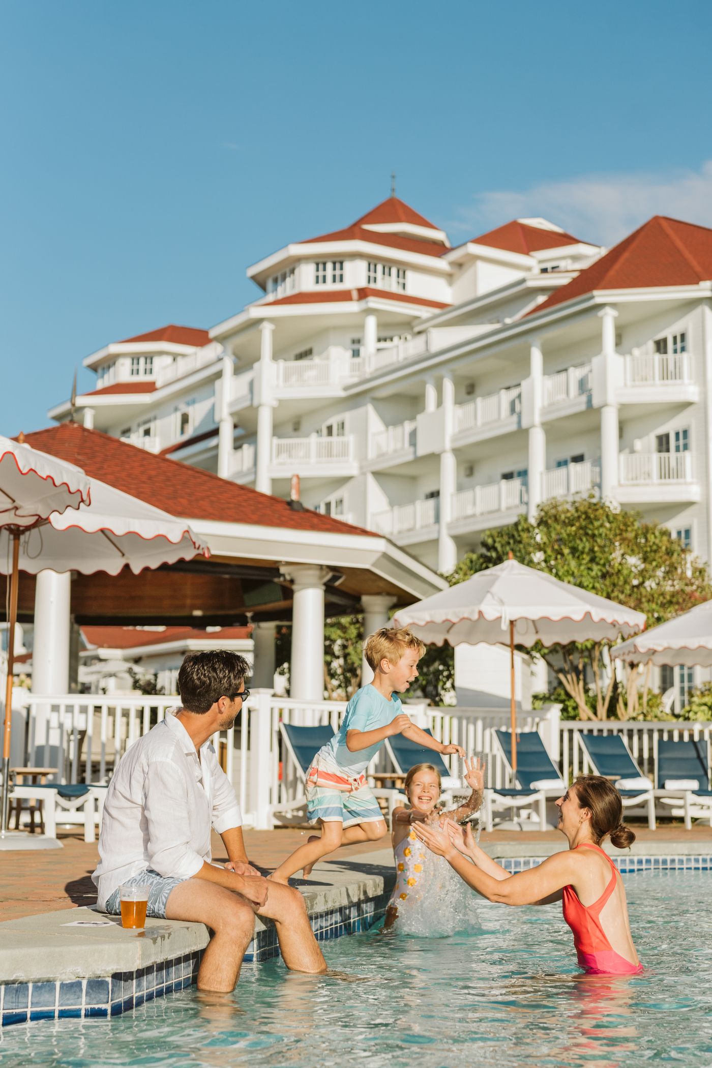 Vacationing family laughs as young boy jumps into pool into waiting mother's arms