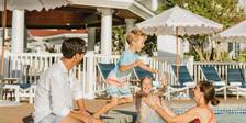 Vacationing family laughs as young boy jumps into pool into waiting mother's arms