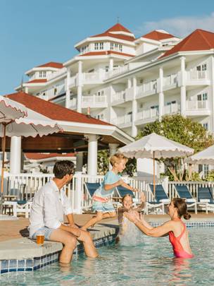 Vacationing family laughs as young boy jumps into pool into waiting mother's arms