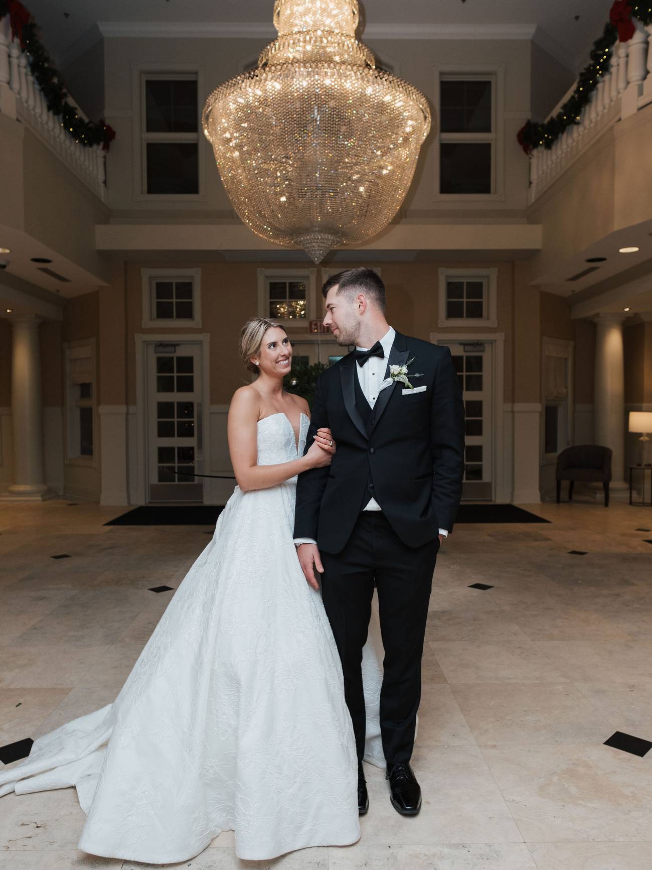 Newlywed couple smiles in front of Inn at Bay Harbor chandelier