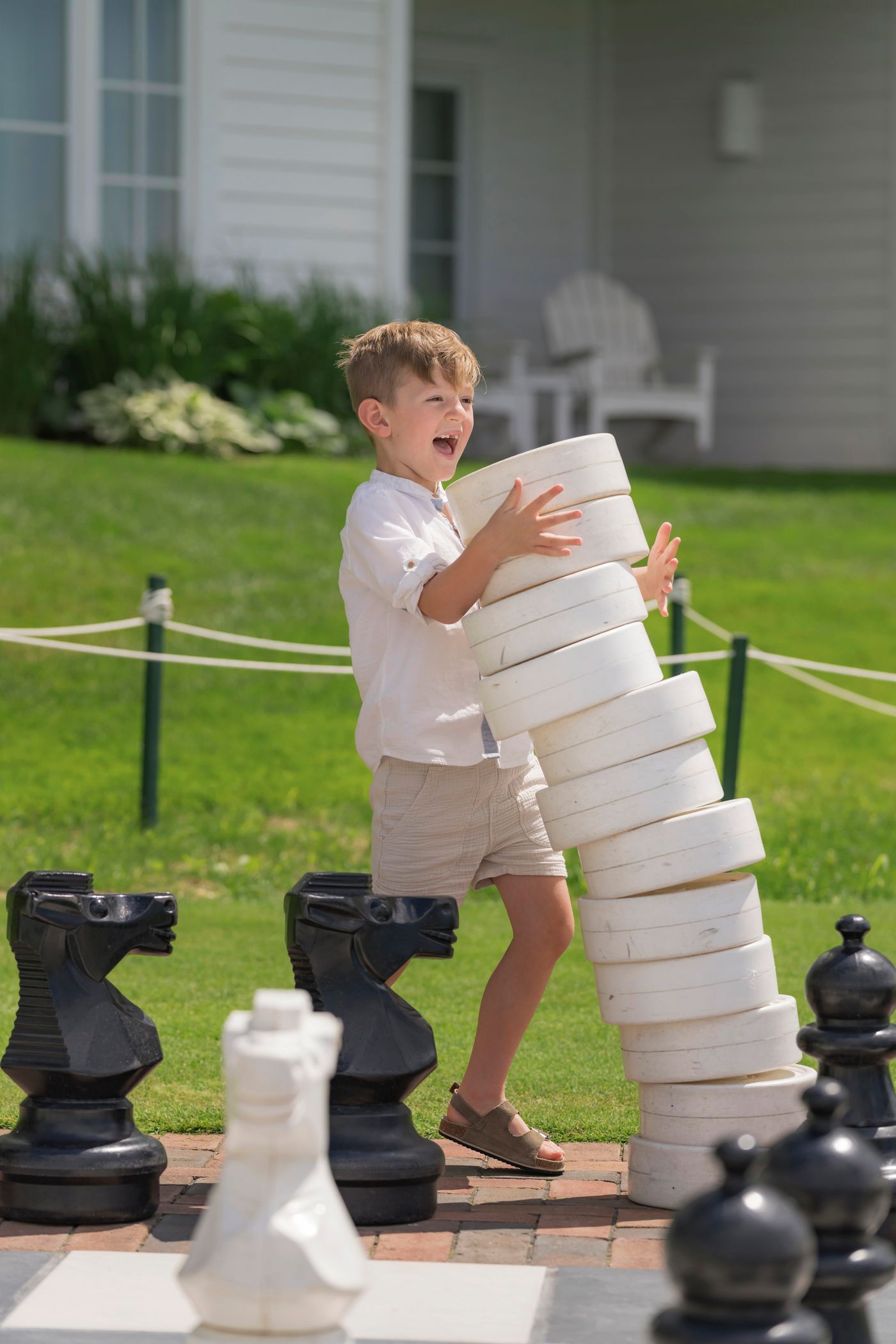 Young boy laughing as he holds stack of giant checkers, Inn at Bay Harbor chess board