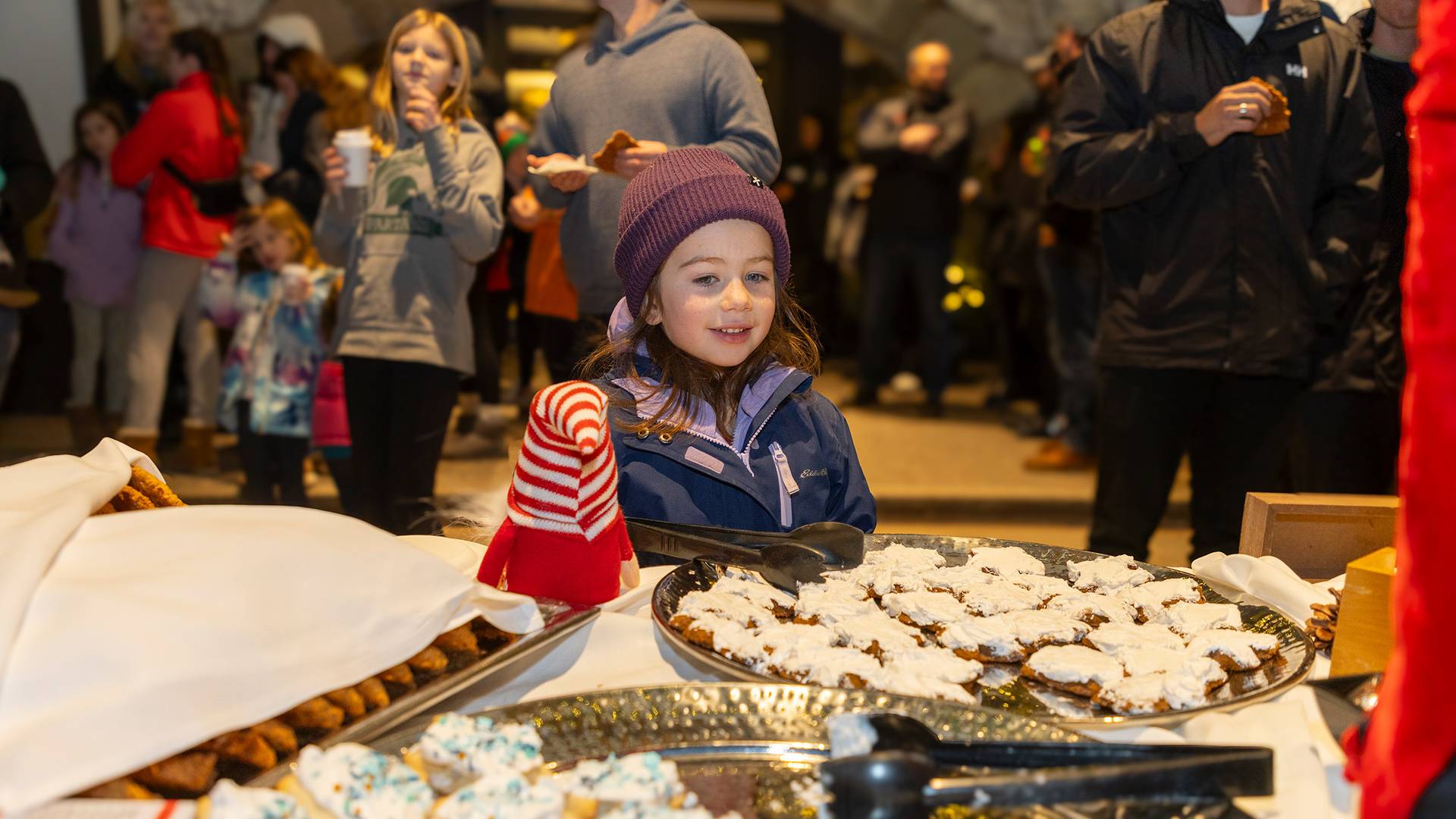 A little girl in winter gear grabbing a cookie