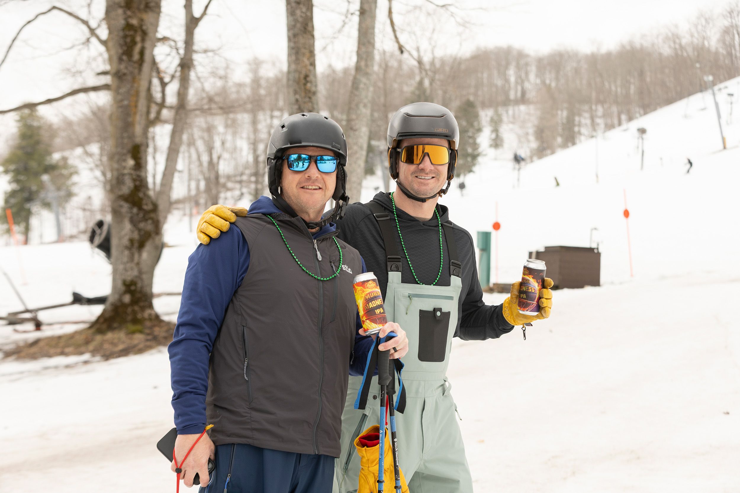 Two skiers in green beads holding beers
