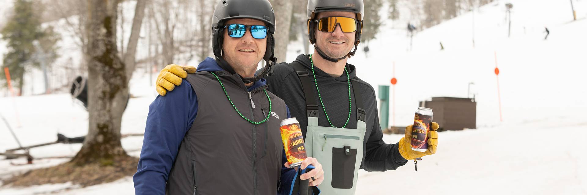 Two skiers in green beads holding beers