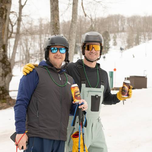 Two skiers in green beads holding beers