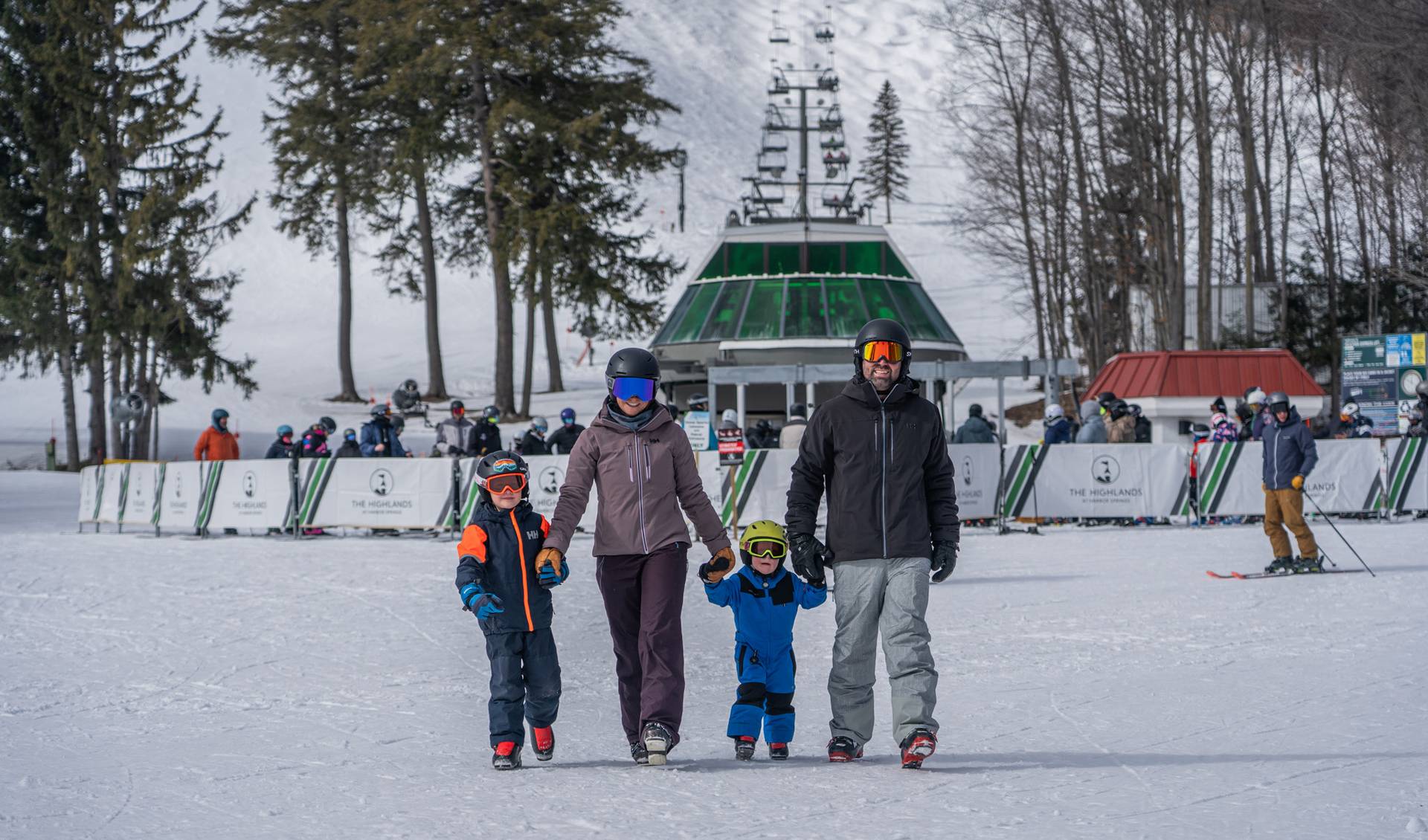 A family in ski gear walking in front of a ski lift