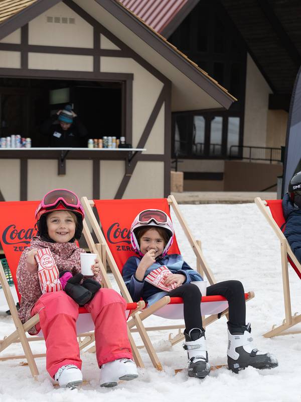 A group in ski gear sitting in red coca-cola chairs outside eating popcorn at The Highlands