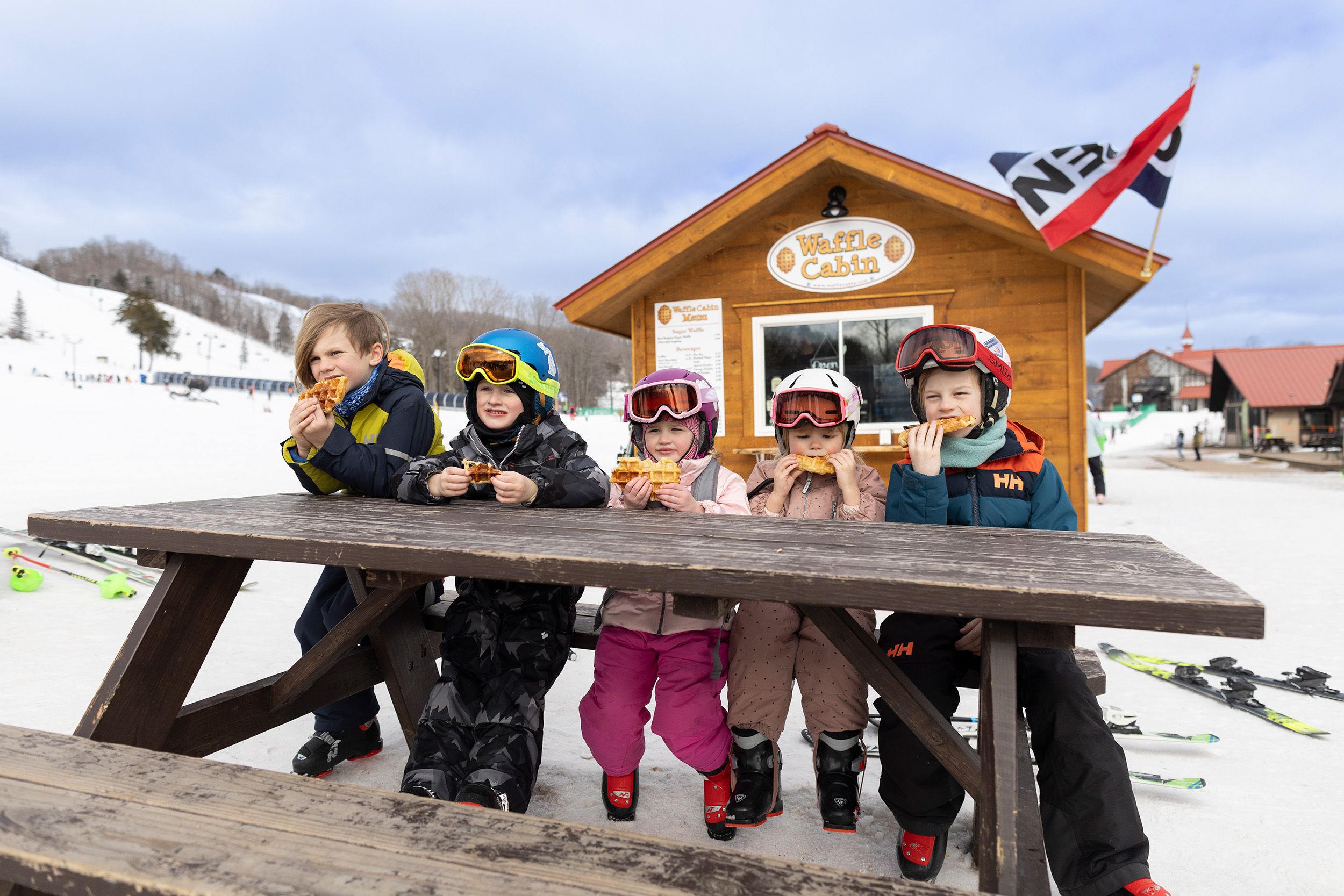 A group of kids eating a waffle in front of the waffle cabin