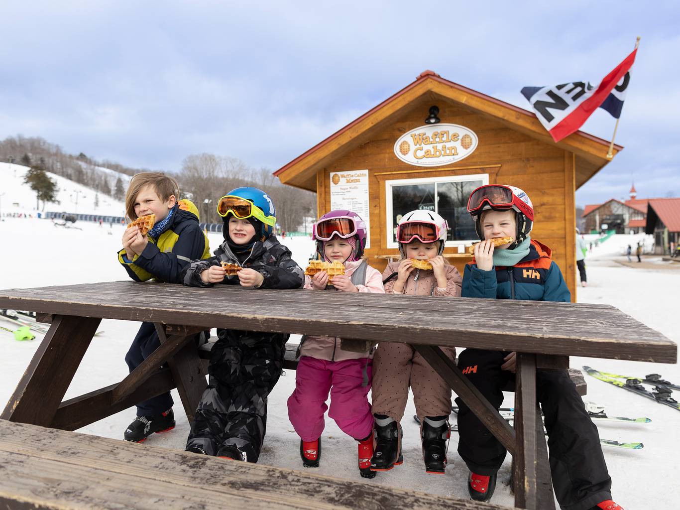A group of kids eating a waffle in front of the waffle cabin