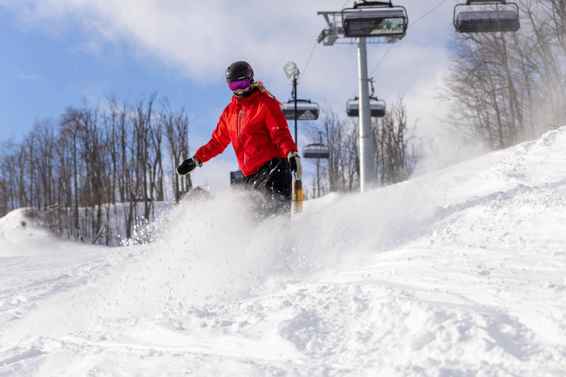 A snowboarder in powder under Camelot 6 chairlift at The Highlands