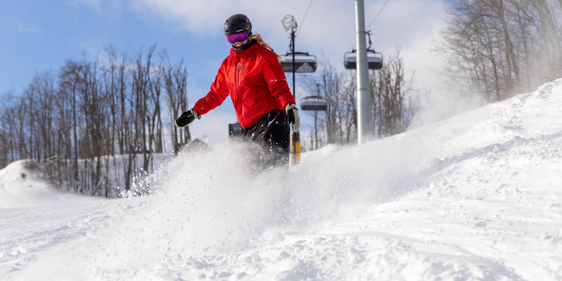 A snowboarder in powder under Camelot 6 chairlift at The Highlands
