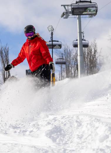 A snowboarder in powder under Camelot 6 chairlift at The Highlands