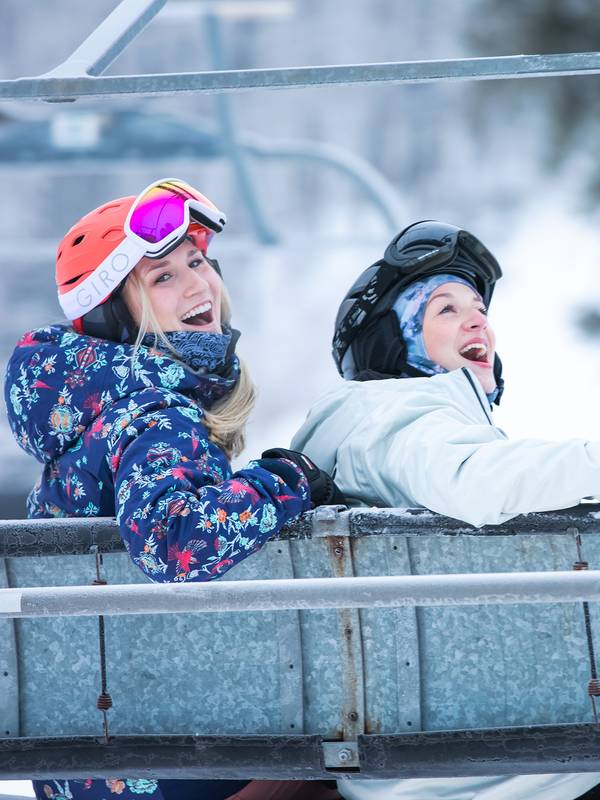 Two women in ski gear posing on a chairlift at The Highlands