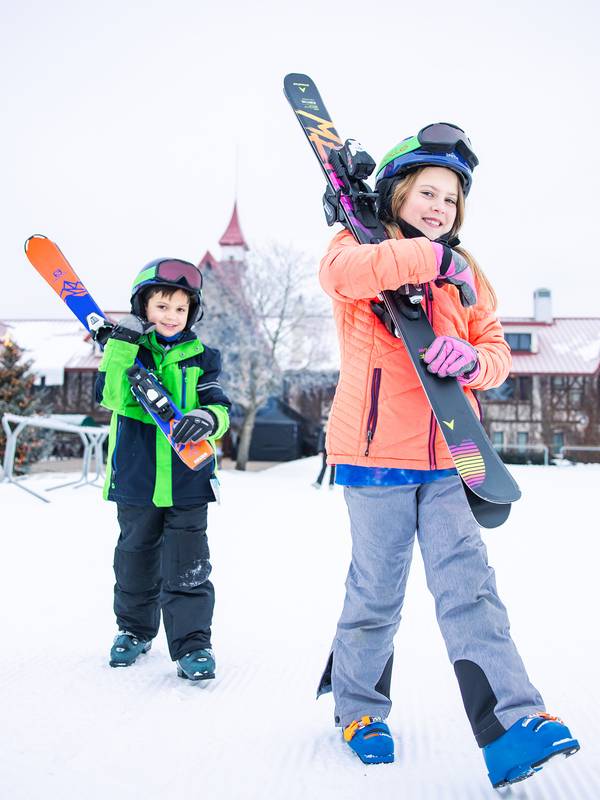 Two kids walking and holding skis