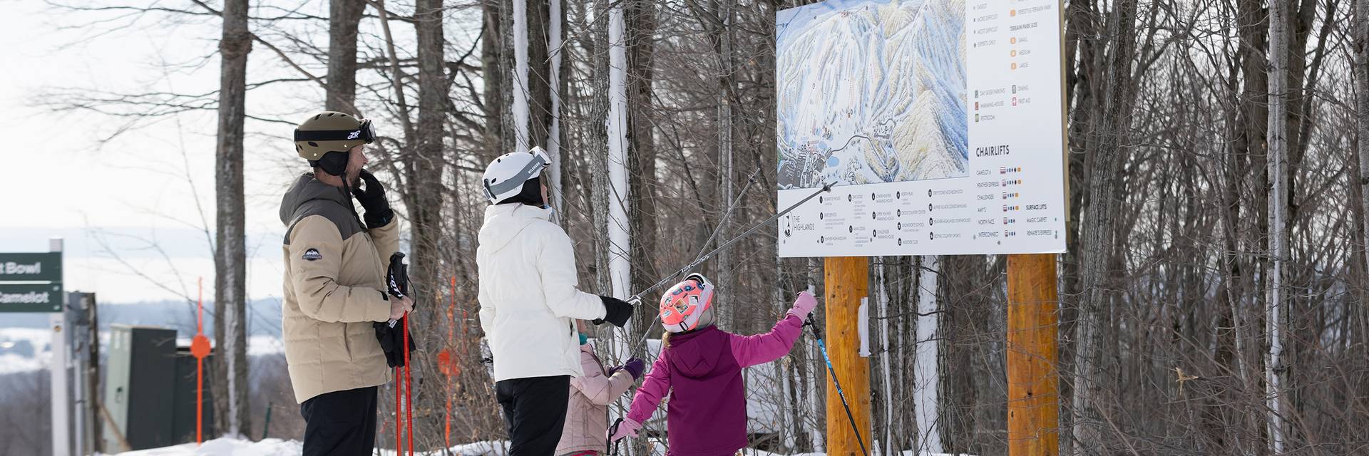 A family in ski gear pointing at a trail map at The Highlands
