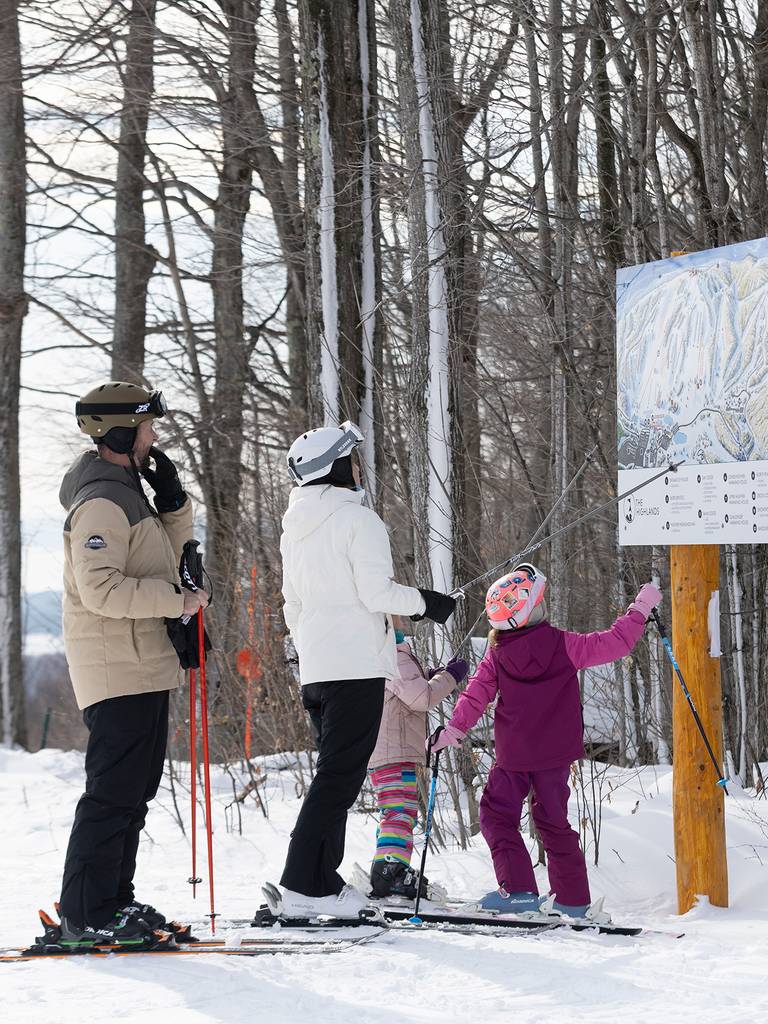 A family in ski gear pointing at a trail map at The Highlands